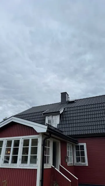 Röd villa med svart tak, takkupa och skorsten under grå himmel