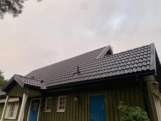Nytt svart pannat tak på en grön trävilla med blå dörrar