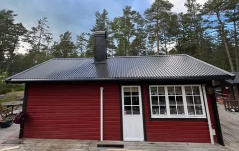 Röd stuga bland tallar med svart plåttak
